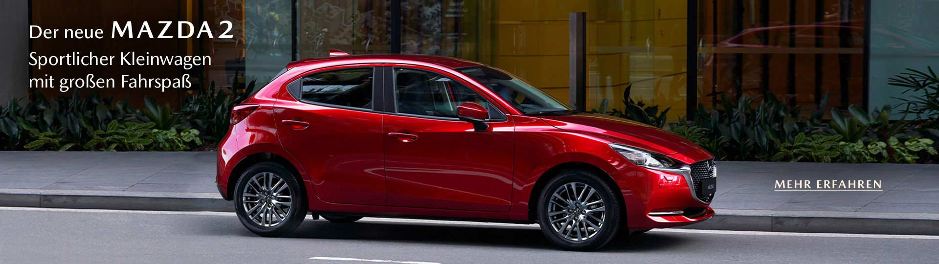 Mazda2 Facelift 2020 in Magmarot Metallic, Seitenansicht. Text: "Der neue Mazda 2, Sportlicher Kleinwagen mit großem Fahrspaß. Mehr erfahren"